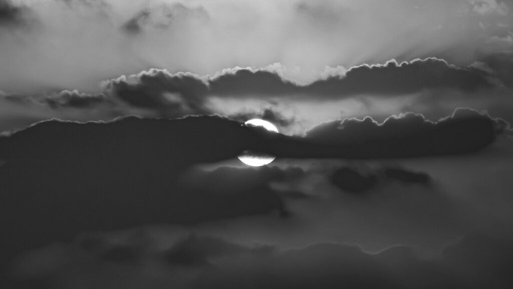 Sole che filtra tra le nuvole sopra un crinale di montagna, bianco e nero